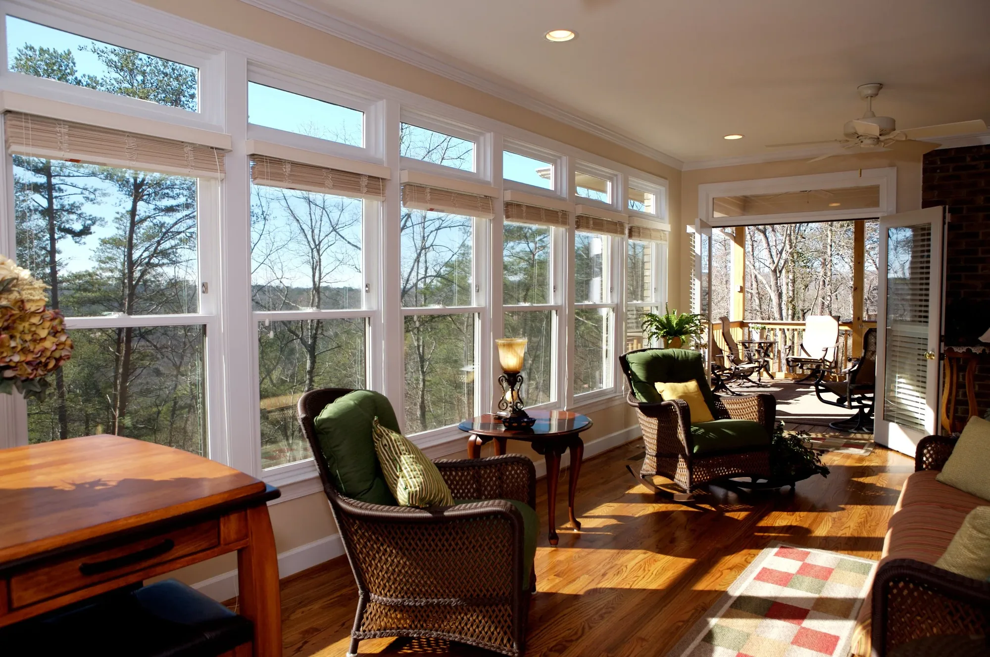 A sunroom lined with windows, wicker seating and a brick wall, looking out into the pines.