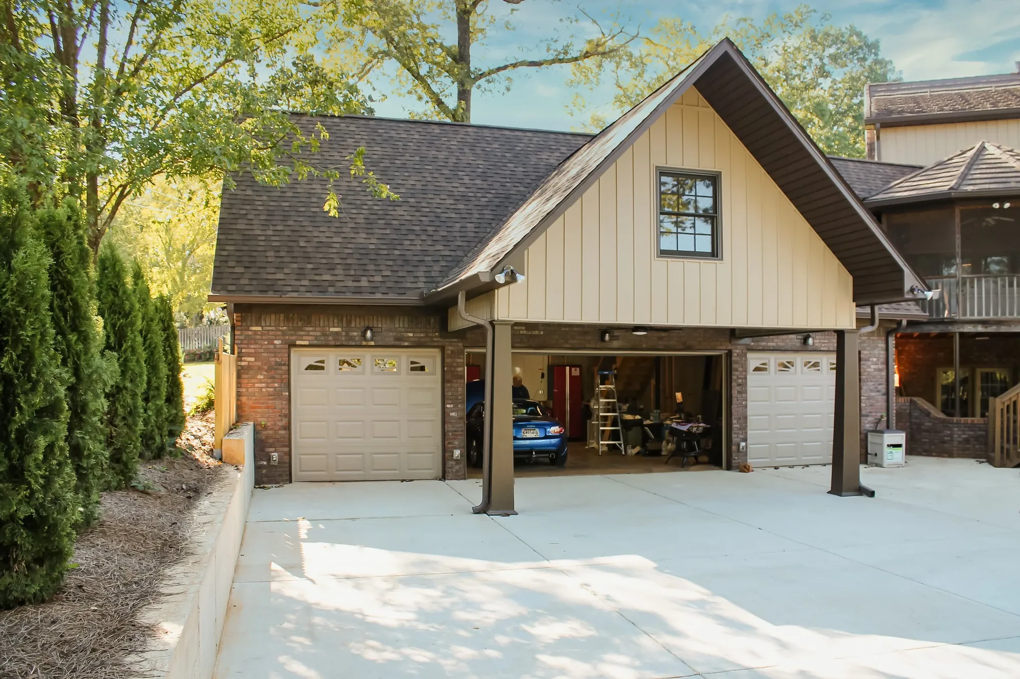 A detached garage and studio building with board and batten gables beside a wooded drive.