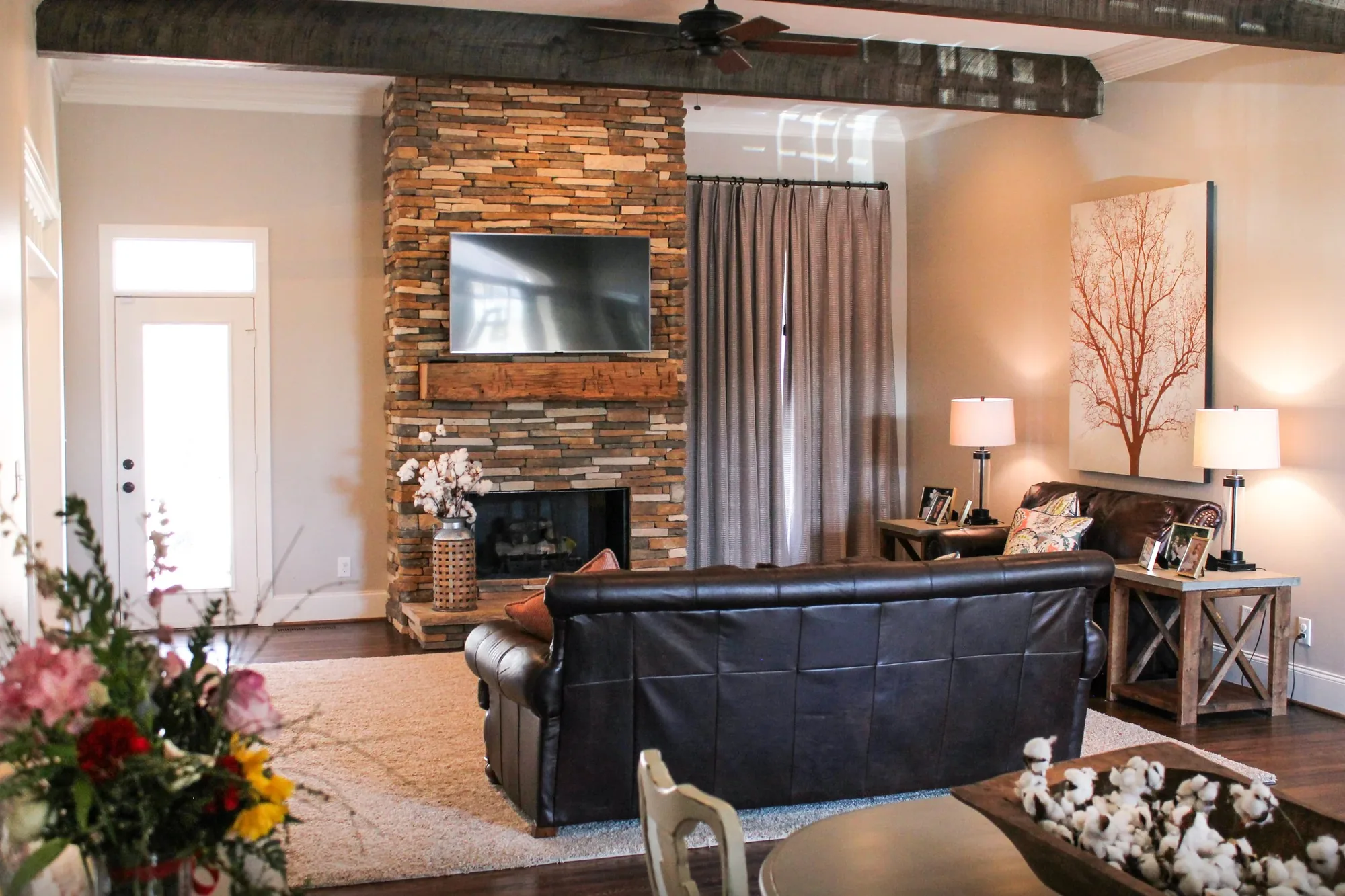 A living room with a floor to ceiling stone fireplace and exposed beam.